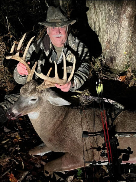 Photo d'un homme en tenue de camouflage avec un arc tenant les bois d'un grand mâle récolté.