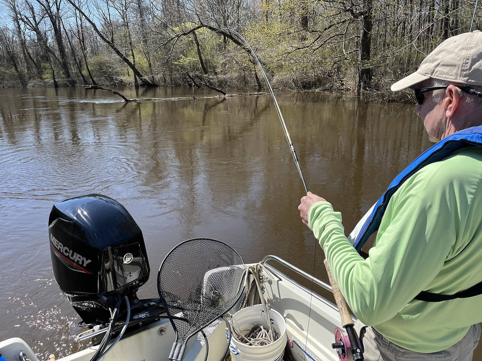 Une photo d'un homme debout dans un bateau avec une canne à pêche à la mouche penchée au-dessus de l'eau.