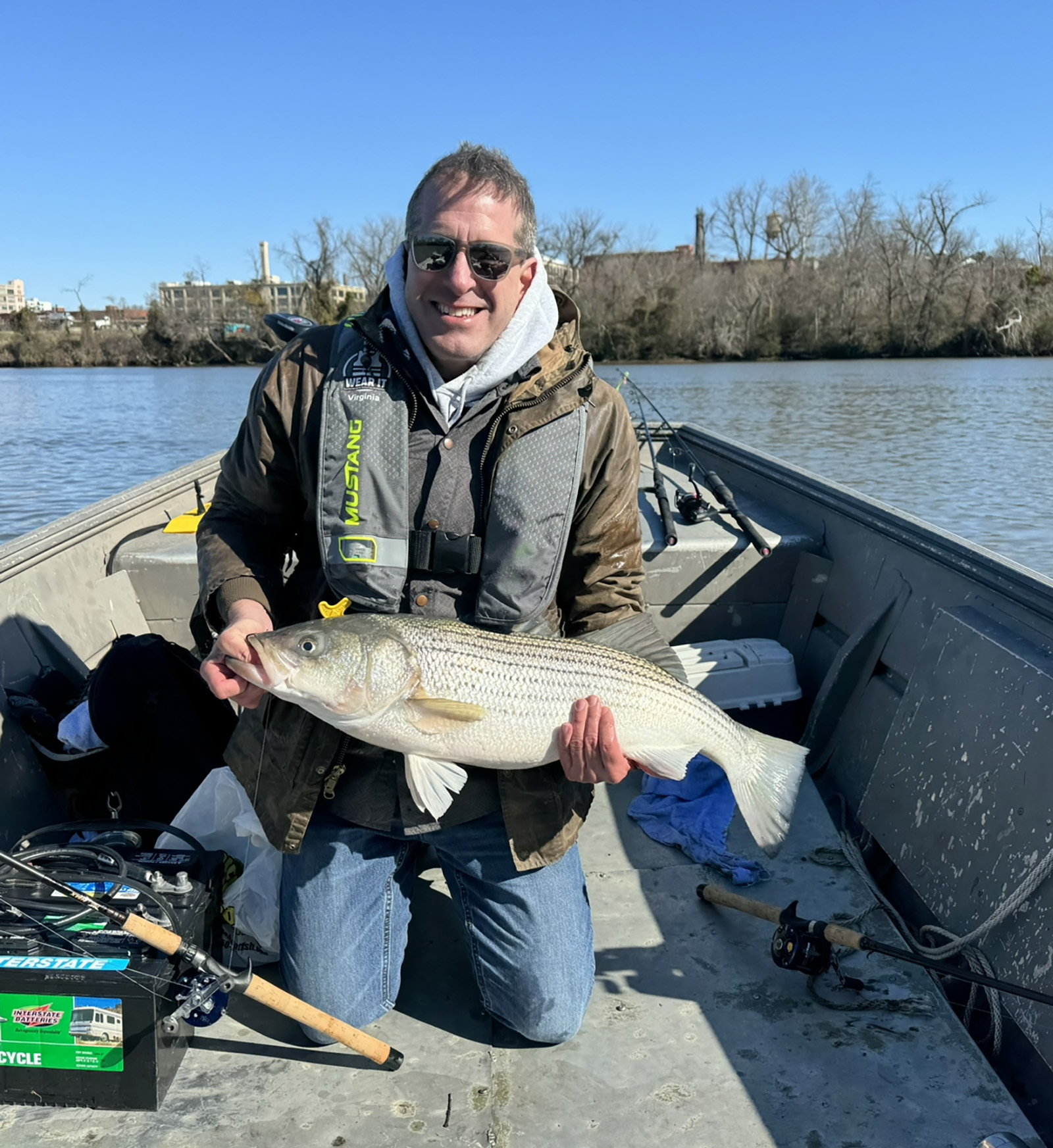 Une photo d'un homme agenouillé à la proue d'un bateau sur la rivière, tenant un grand bar rayé. 
