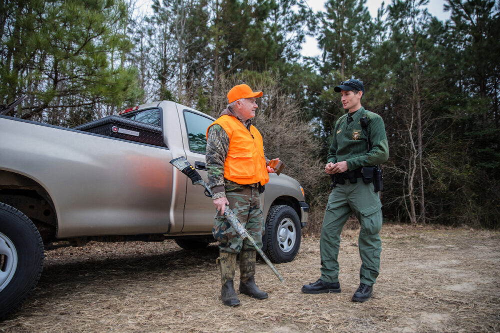 Image d'un chasseur équipé d'un camion et d'un gilet de visibilité orange discutant avec un homme en vert qui est un agent de la police de la conservation.