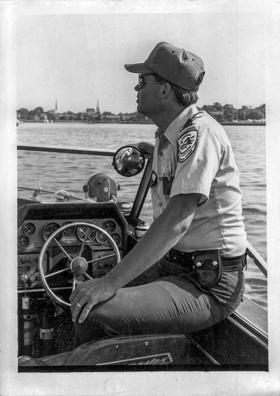 Photo en noir et blanc d'un homme en uniforme de garde-chasse pilotant un petit bateau.