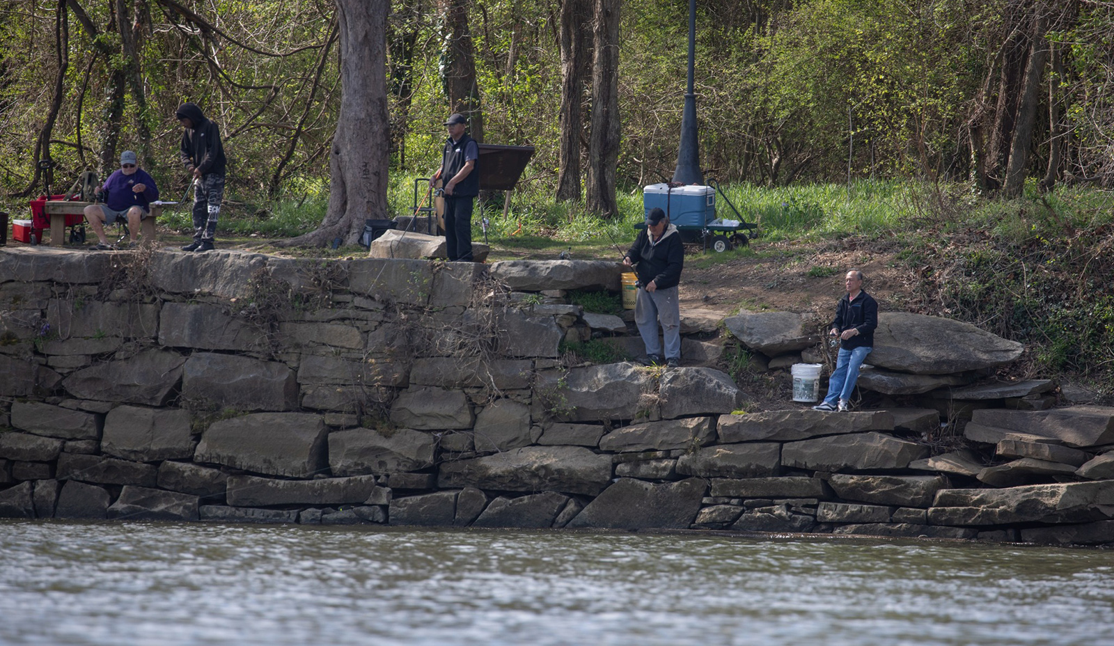 Une photo de personnes debout et assises au bord d'une rivière en train de pêcher.