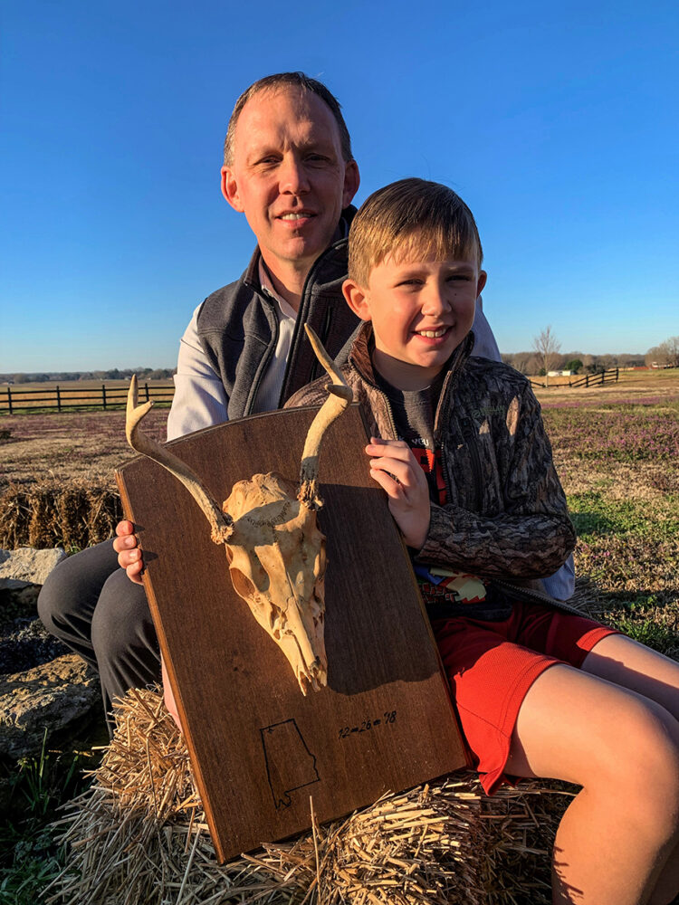 Image d'un homme et de son soleil tenant un crâne de cerf encadré, le premier cerf qu'ils ont abattu ensemble.
