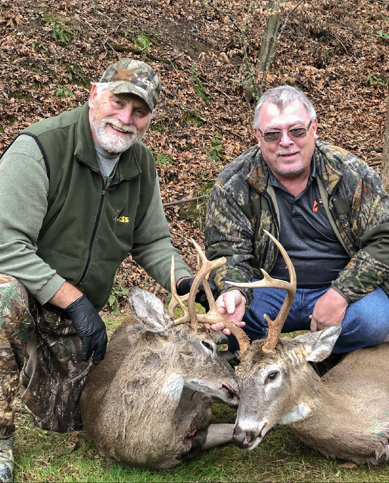 Une photo de deux hommes s'agenouillant et brandissant les bois de deux cerfs de Virginie.