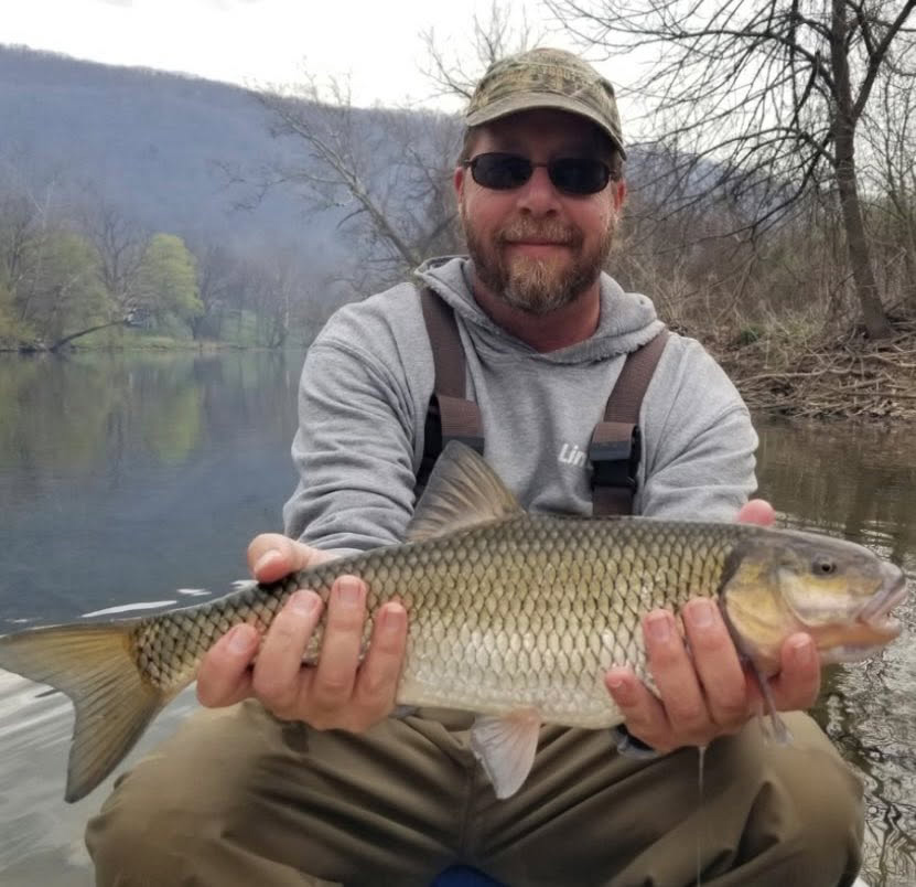 Photo d'un homme tenant un grand poisson-chasseur avec une rivière en arrière-plan.