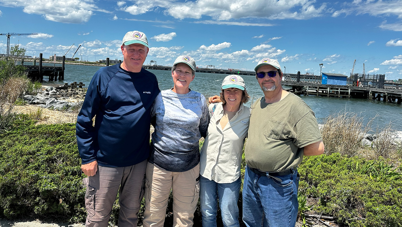 Une photo de quatre personnes souriantes se tenant sur la plage d'une île avec de l'eau en arrière-plan.