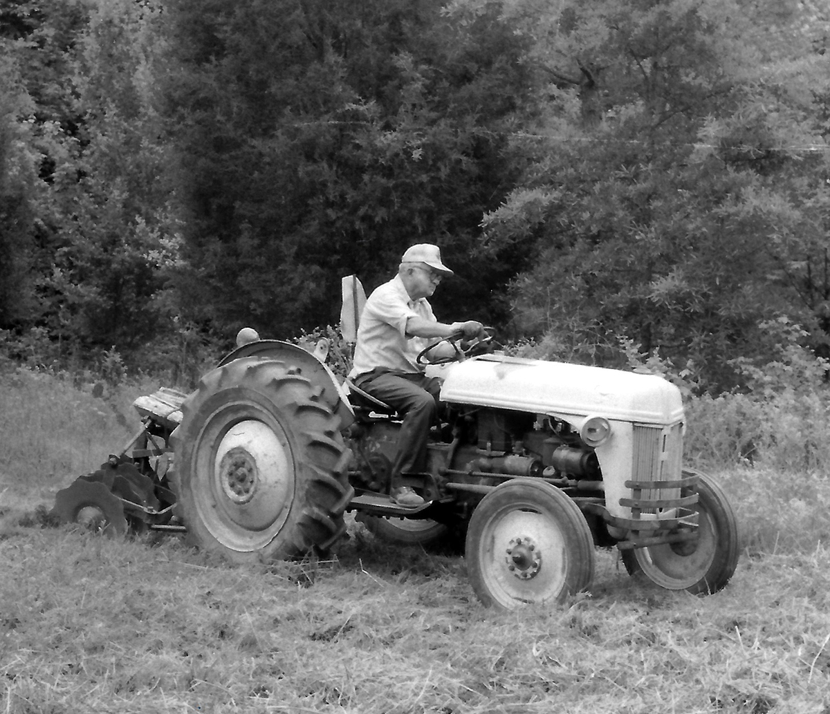 Image en noir et blanc d'un homme avec un tracteur labourant un champ.