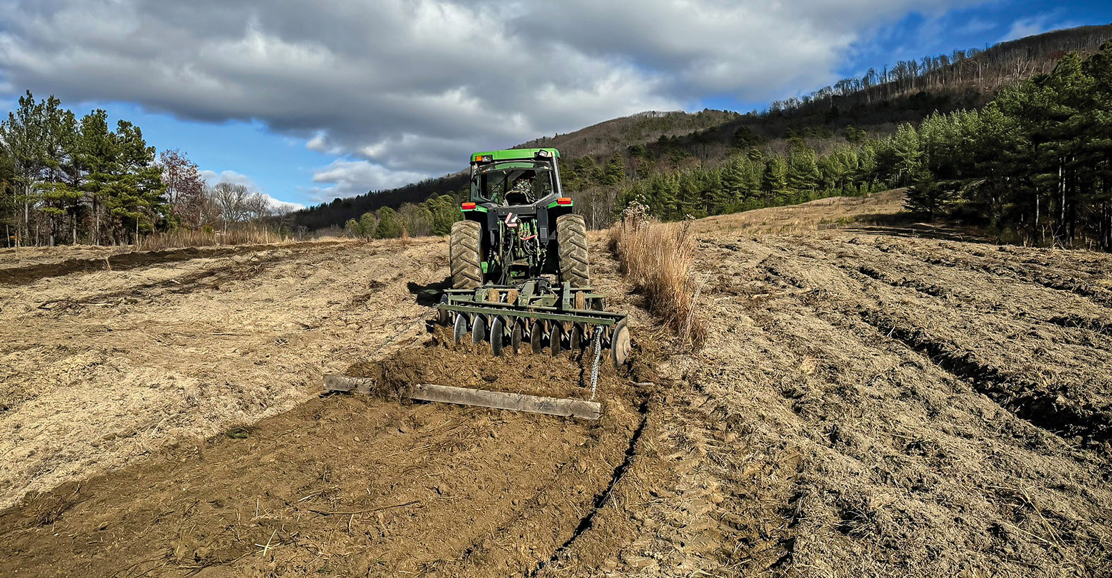 Une photographie d'un tracteur tirant une herse à disques sur un champ de terre nue.