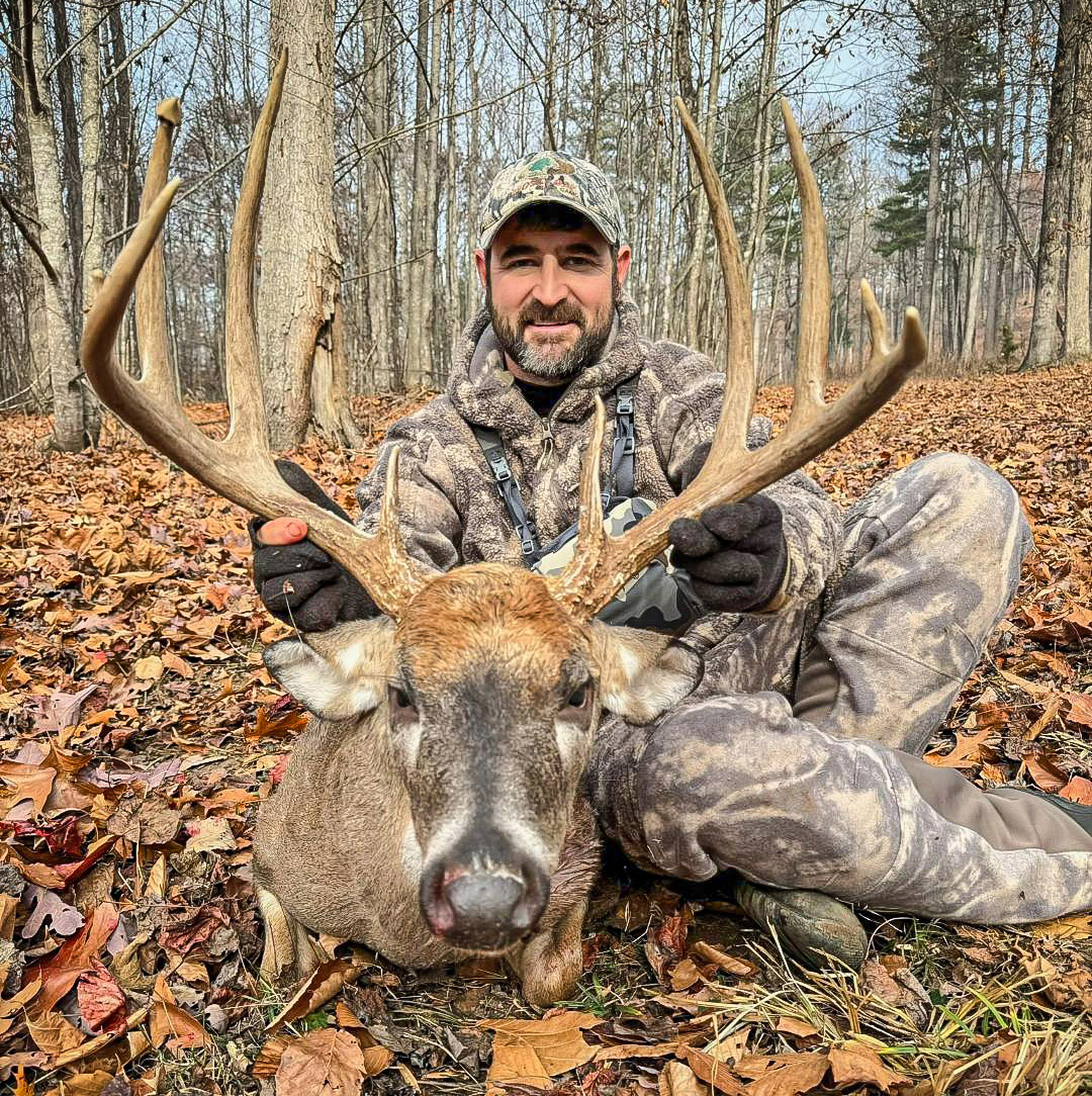 Une photo d'un homme en tenue de camouflage et d'un grand cerf à queue blanche.