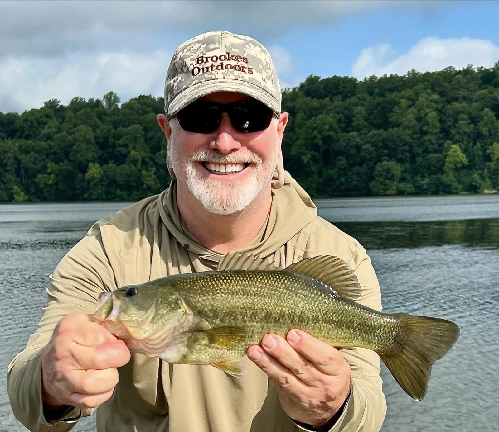 Un homme tenant un achigan à grande bouche devant une rivière.