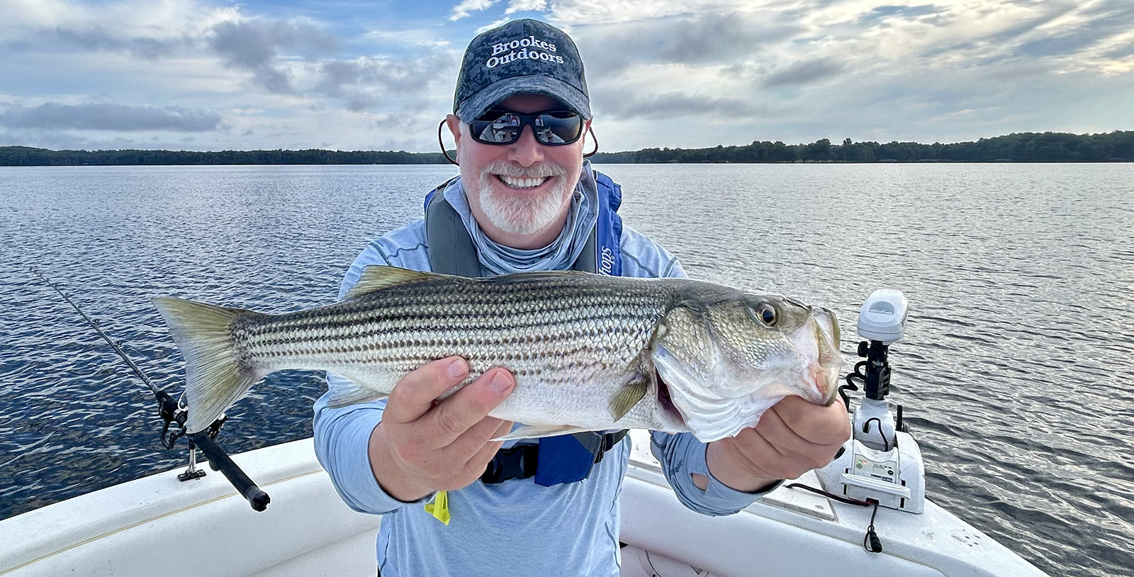 Un homme assis sur un bateau, brandissant un grand bar rayé et souriant.