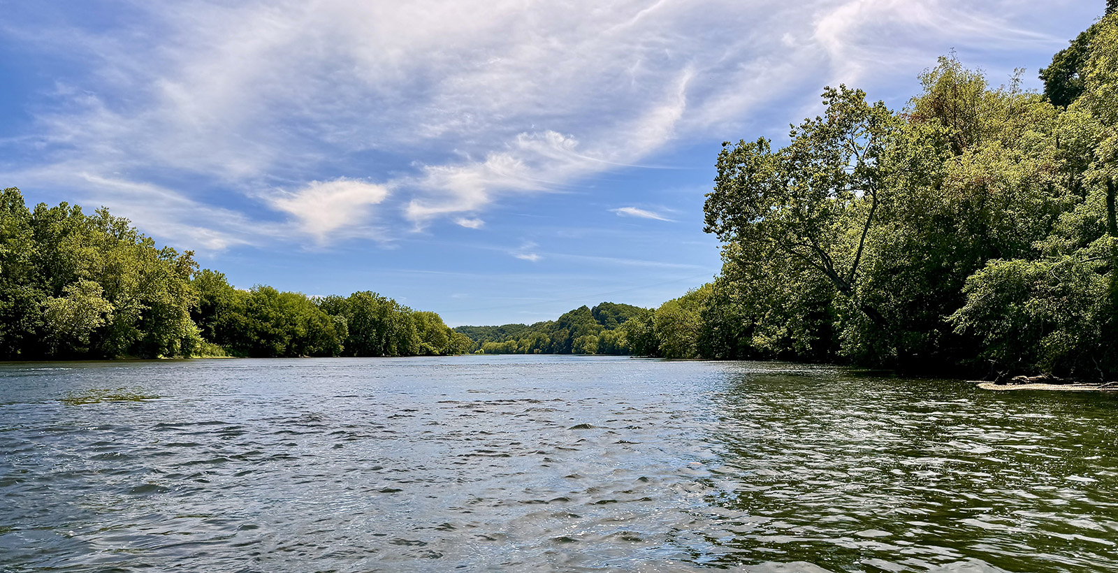 Une photo d'une rivière pittoresque avec des arbres sur les berges et un ciel bleu.