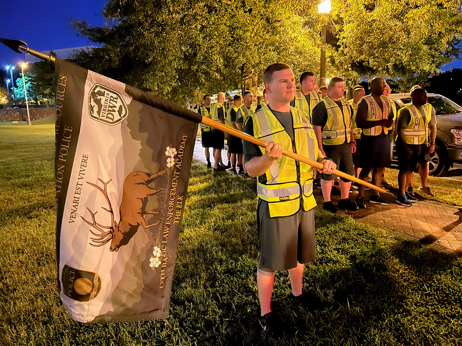 Une photo prise à la lumière de l'aube d'un groupe de jeunes hommes et femmes se préparant à courir. L'homme à l'avant tient un drapeau DWR orné d'un élan.