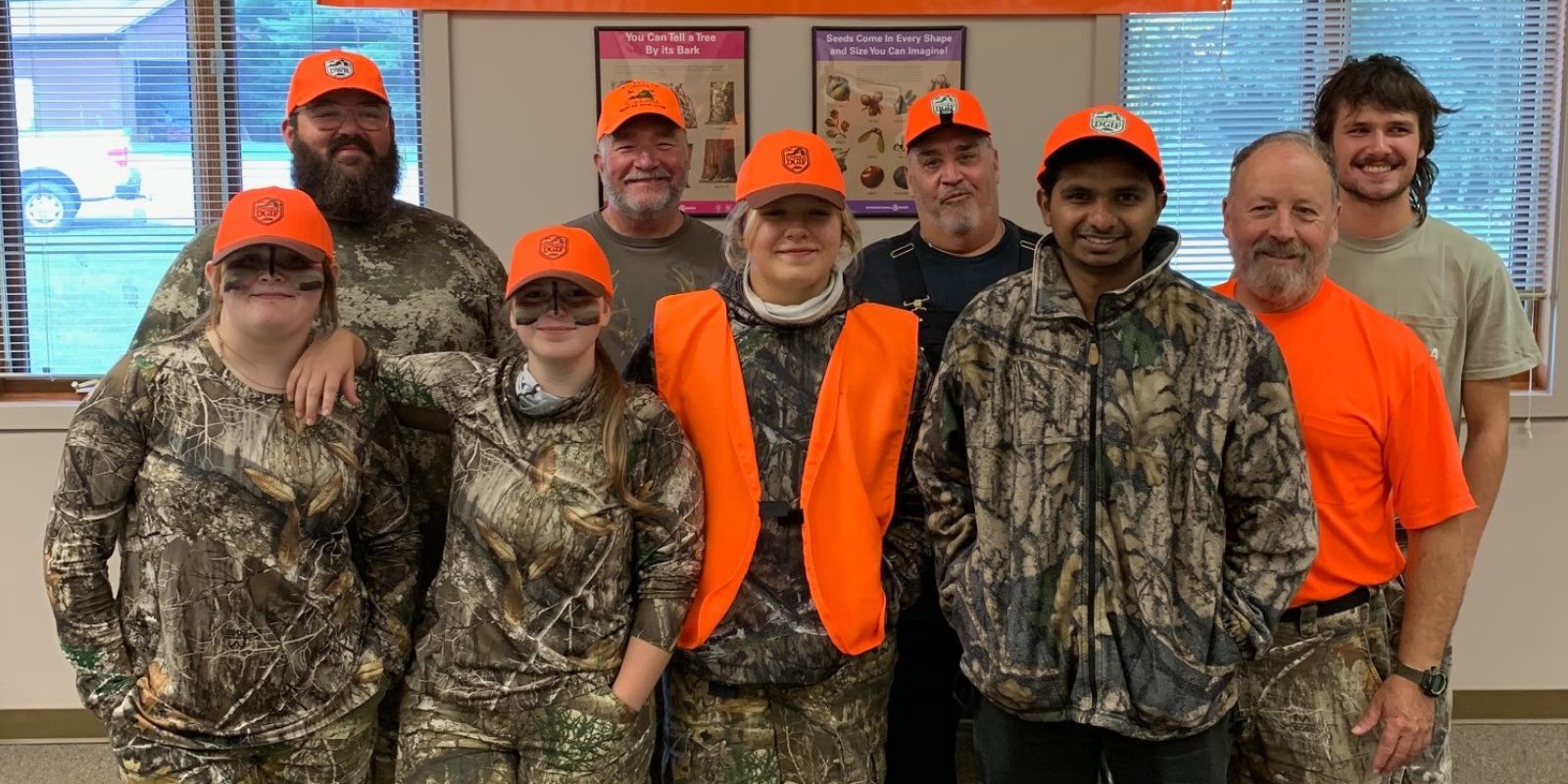 Un groupe de huit hommes et femmes se tenant ensemble, tous vêtus de camouflage et d'orange vif. 