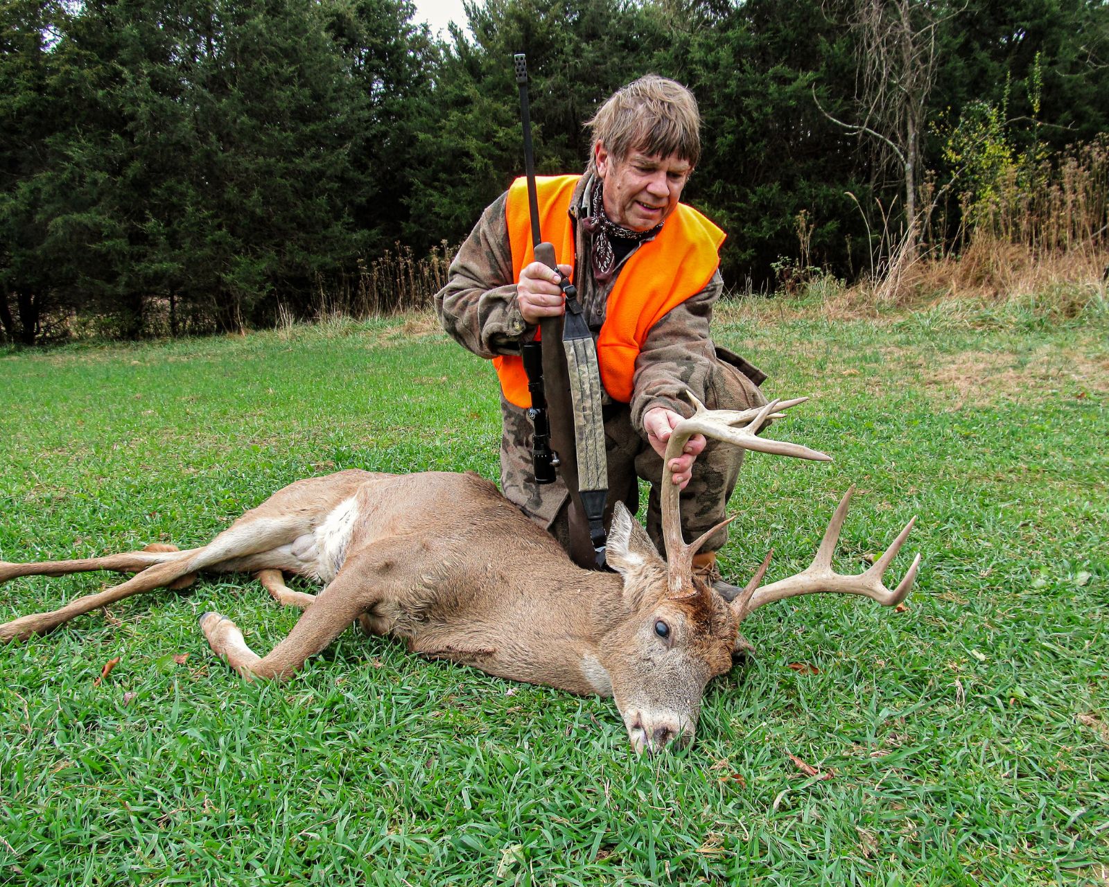 Un chasseur posant avec son fusil et un grand cerf avec bois qu'il a abattu.