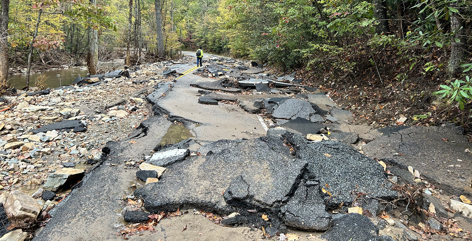 Une photo d'une route détruite, avec des morceaux d'asphalte éparpillés, à côté d'un ruisseau.