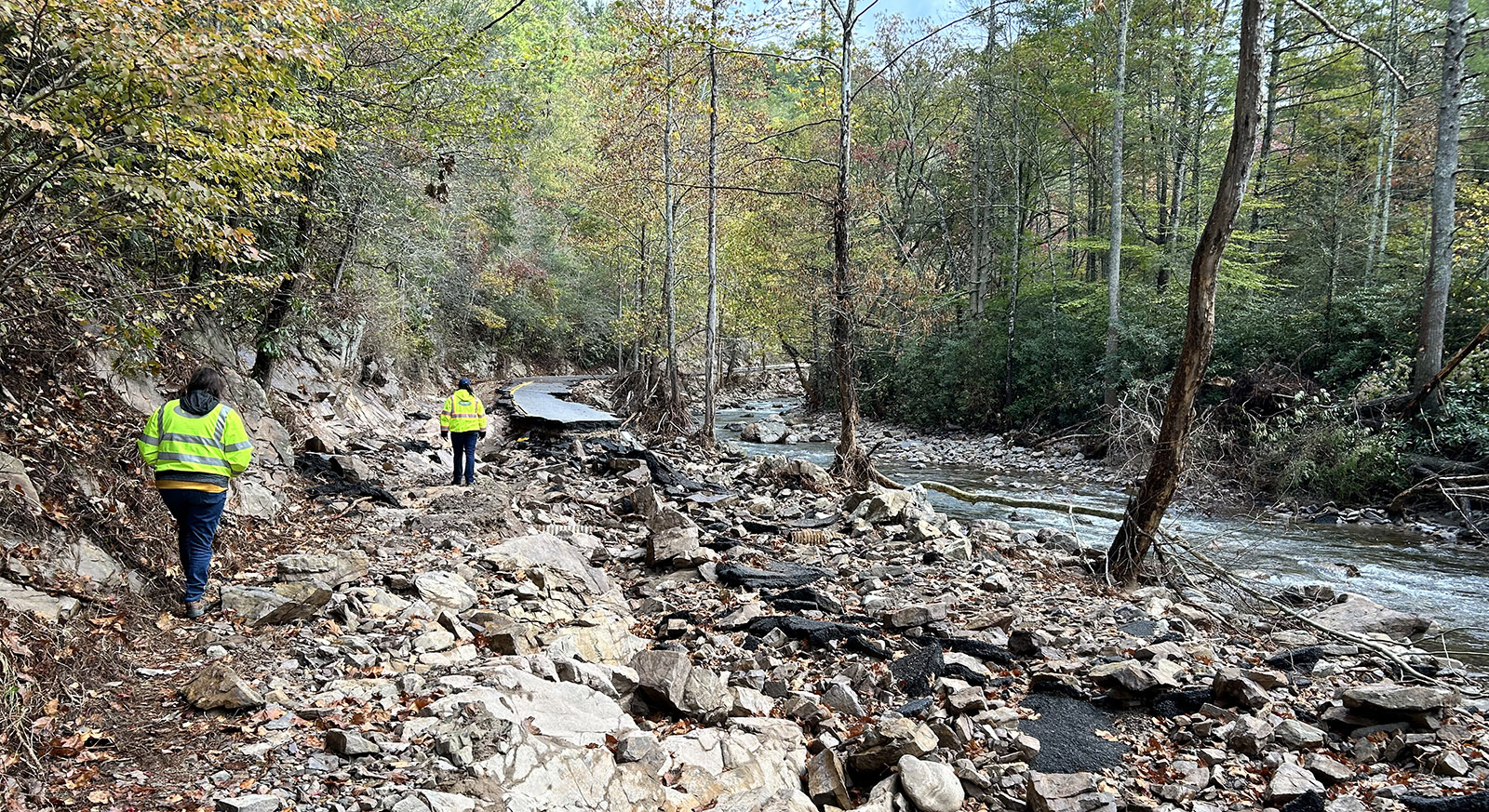 Une photo de deux personnes portant des gilets réfléchissants marchant sur une route détruite près d'un ruisseau.