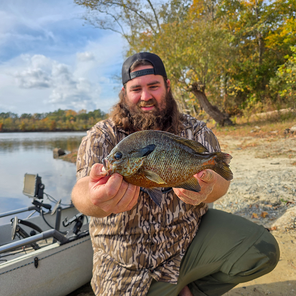 Une photo d'un homme agenouillé devant un kayak sur le rivage, brandissant un grand poisson lune à poitrine rouge et souriant.