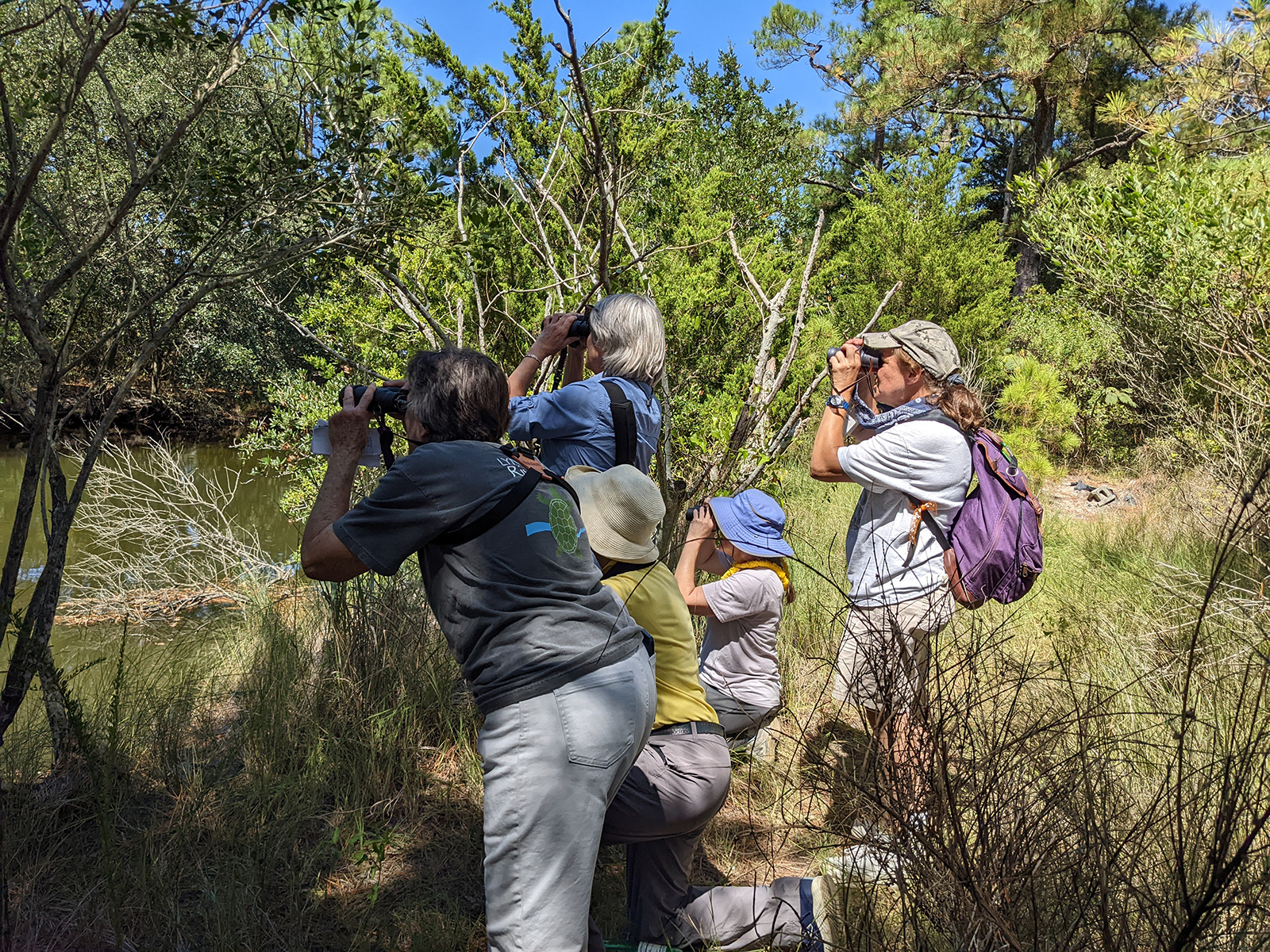 Photo d'un groupe de personnes au bord d'une rivière, regardant l'eau à travers des jumelles.