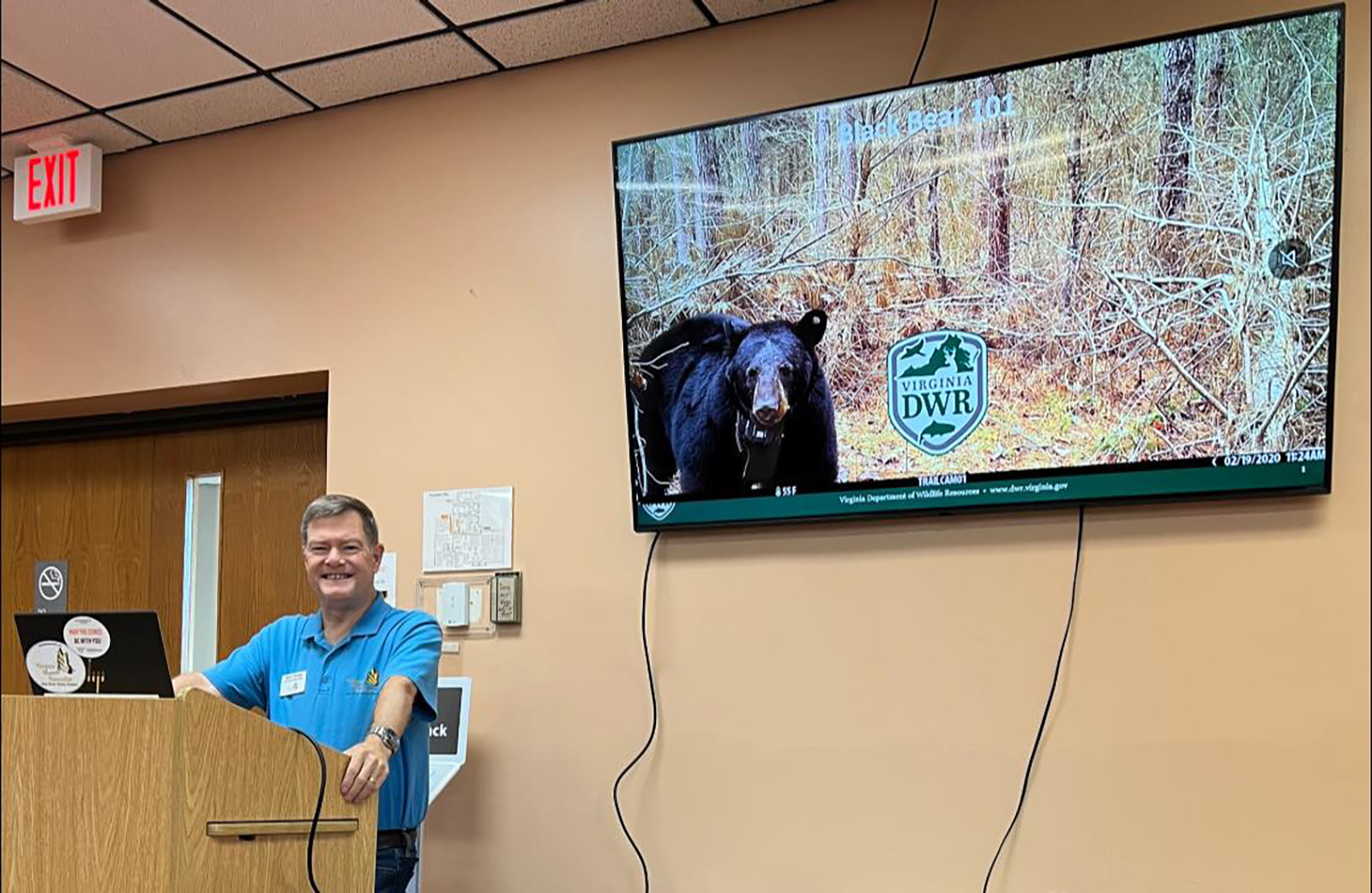 Photo d'un homme derrière un pupitre faisant une présentation, avec une photo d'un ours noir sur l'écran derrière lui.