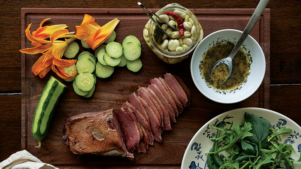 Image d'une portion d'oie fumée, d'hémérocalles, de concombre, de roquette et de fèves au vinaigre.