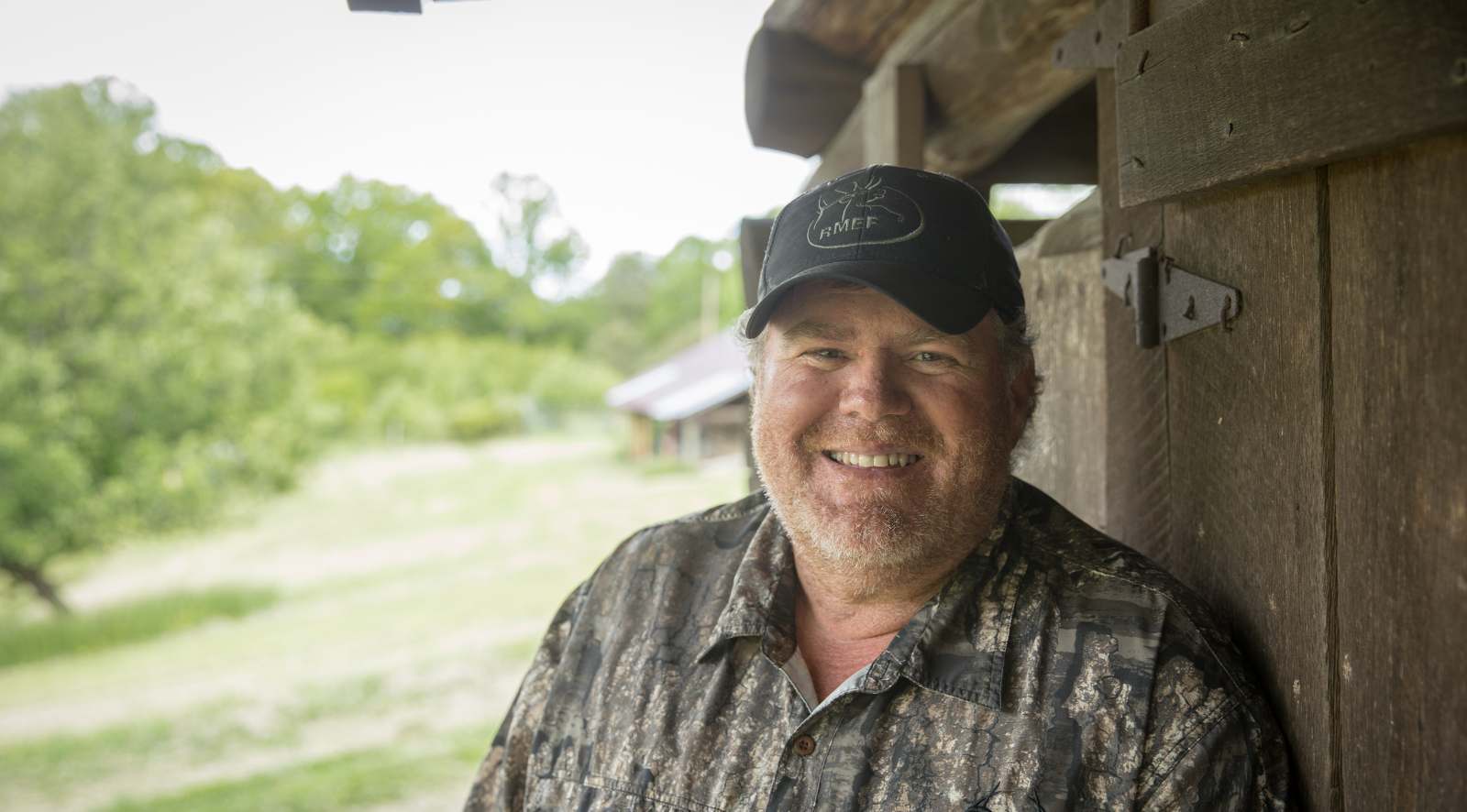 Photo de portrait d'un homme barbu debout à l'extérieur, près d'un bâtiment en bois brut.