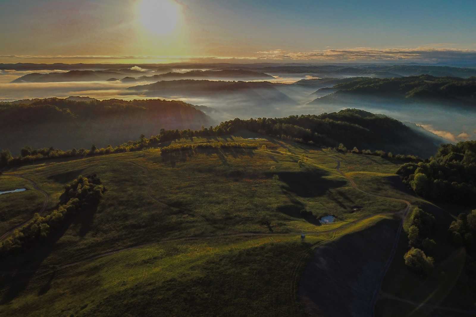 Une magnifique photo aérienne de montagnes boisées entourées de brouillard.