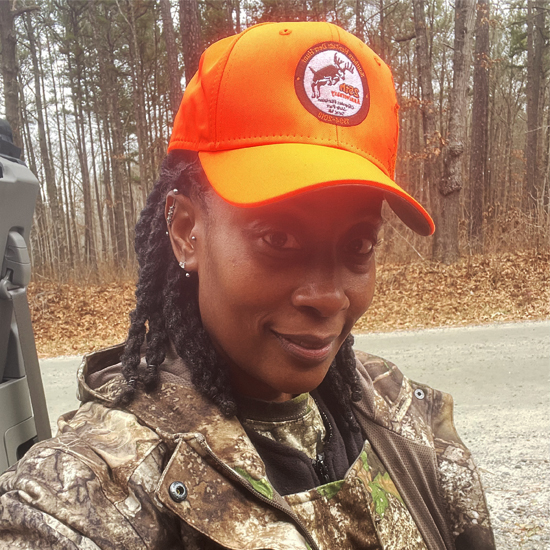 Une photo d'une femme en tenue de camouflage avec une casquette orange vif.