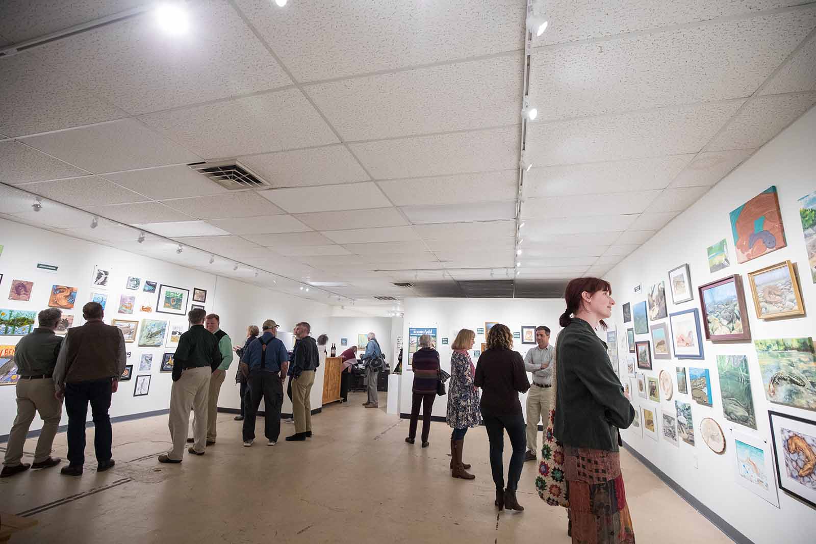 Des personnes rassemblées dans une galerie d'art, regardant diverses œuvres d'art sur le mur