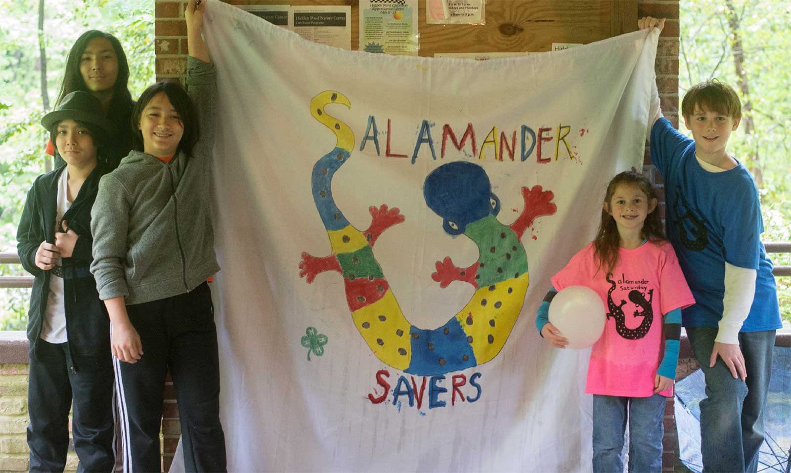 Une photo de plusieurs enfants brandissant une feuille sur laquelle est écrit "salamander savers !" Cela fait partie de l'initiative de conservation de la jeunesse visant à sensibiliser le public aux salamandres et à leur situation critique.