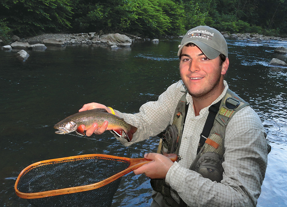 Image d'un pêcheur tenant un filet et une truite brune devant une rivière.