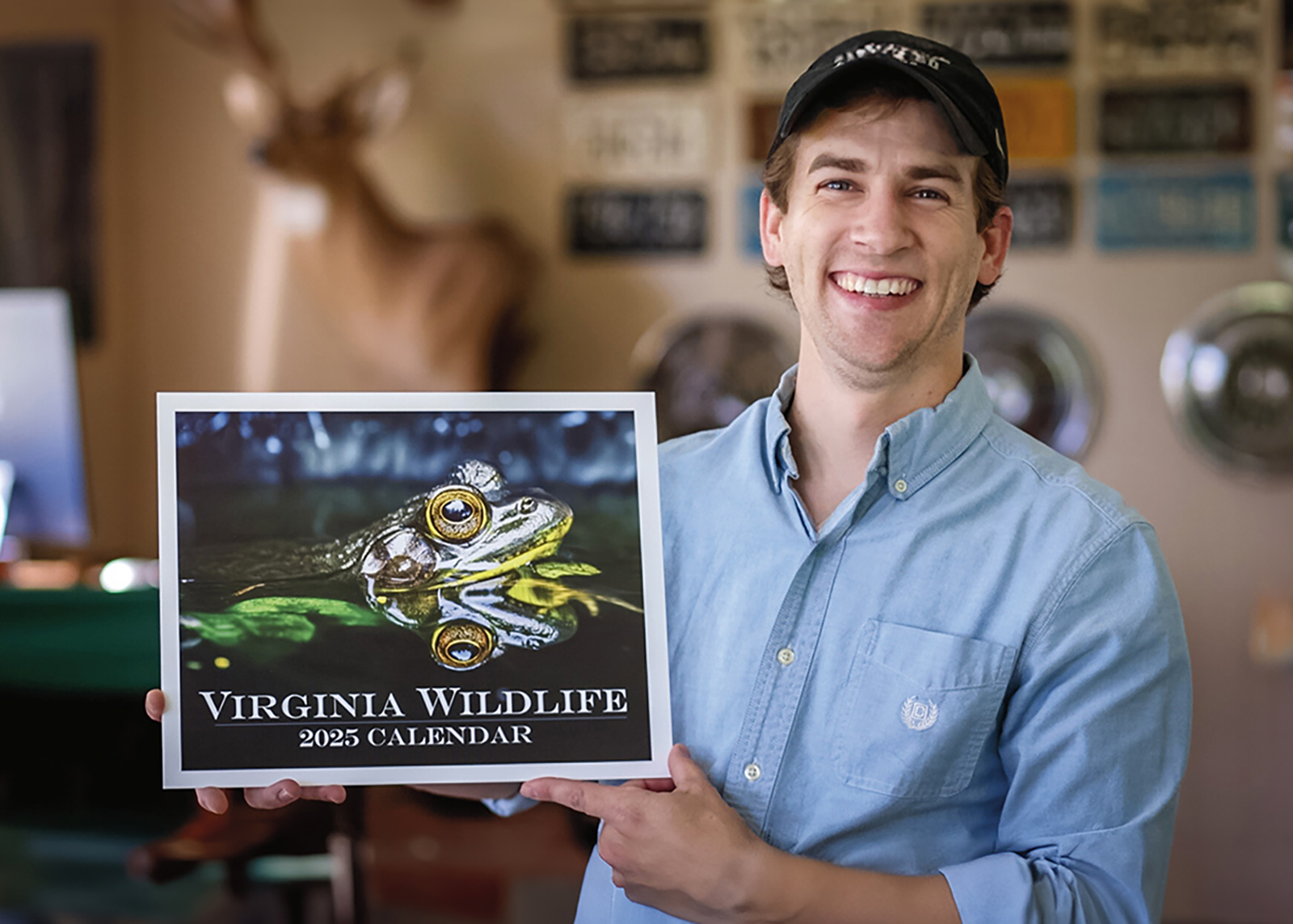 Photo d'un homme au large sourire tenant un calendrier Virginia Wildlife avec une grande photo de grenouille sur la couverture.