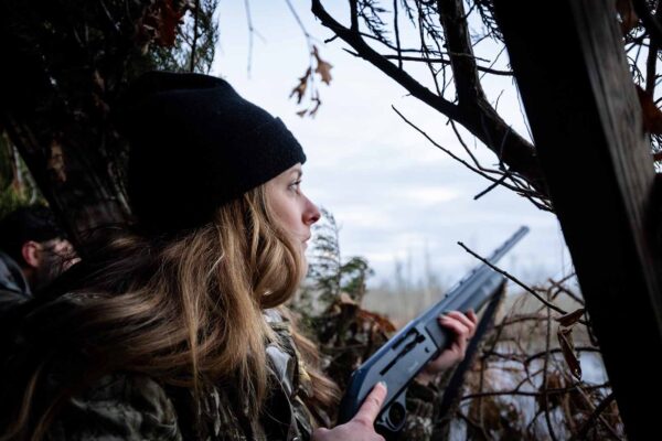 Une femme en tenue de camouflage dans un affût de chasse au bord de l'eau