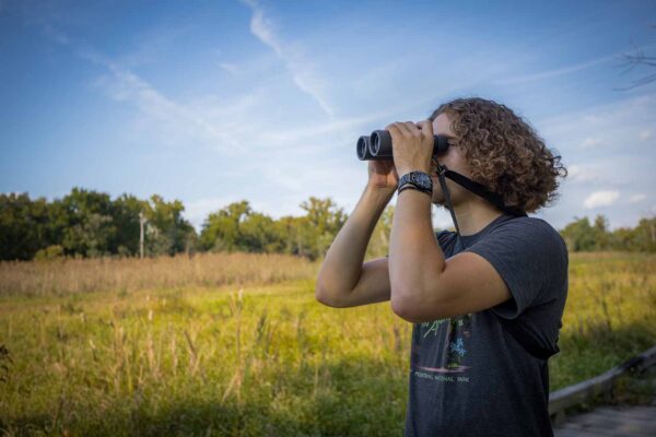 Un homme en t-shirt tenant des jumelles et regardant au loin.