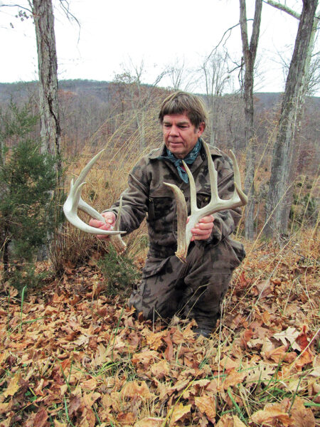 Photo d'un homme tenant deux bois de cerf dans une forêt d'arbres à feuilles caduques.