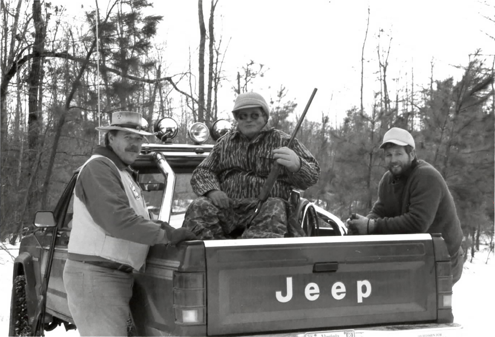 Une vieille photo en noir et blanc de trois chasseurs de cerfs près d'un camion.